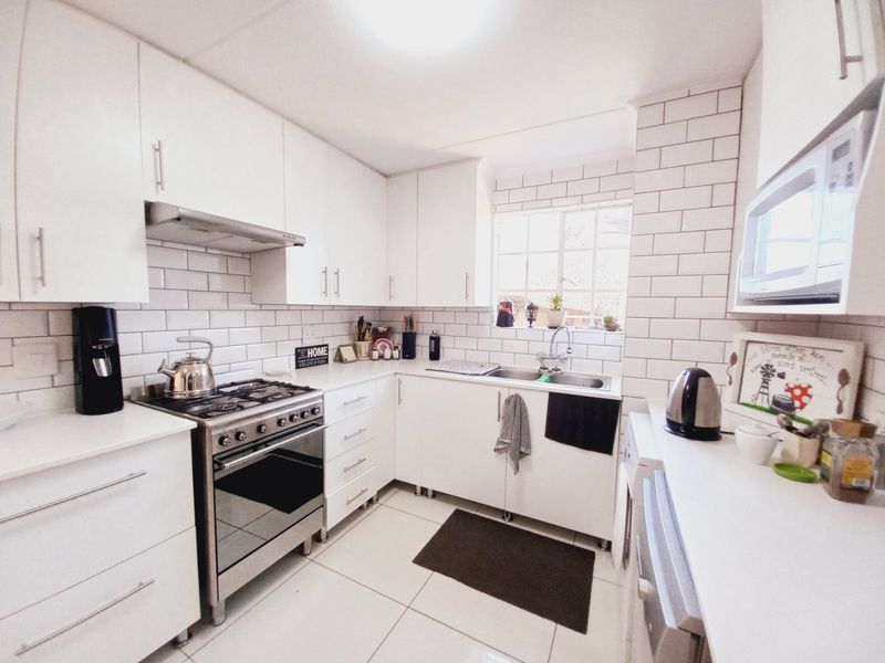 A bright, modern kitchen featuring white cabinetry, subway tile backsplash, stainless steel gas stove, extractor fan, and built-in microwave with tiled flooring.