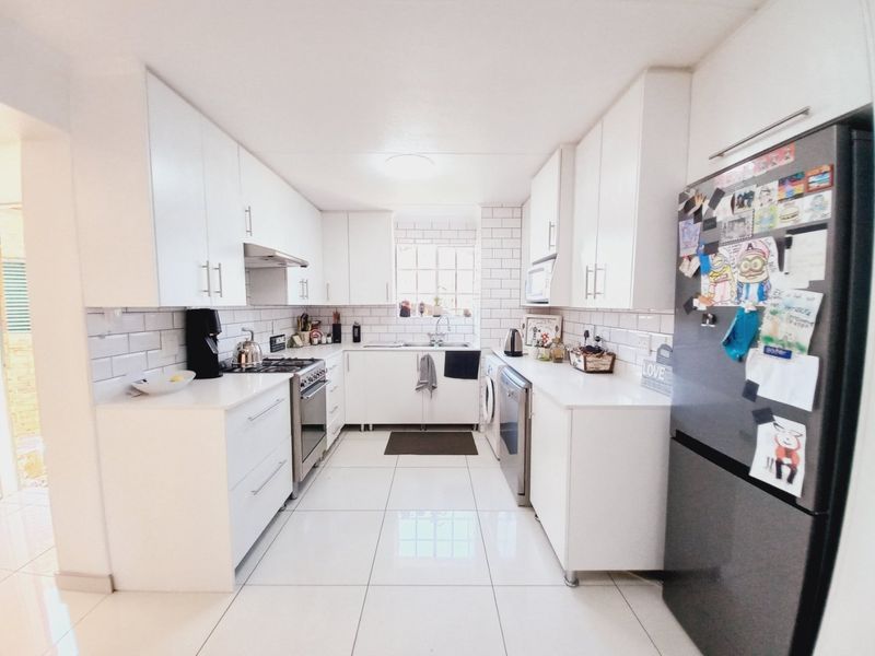 Modern galley-style kitchen featuring white cabinetry, subway tile backsplash, gas stove, and sleek porcelain floor tiles.