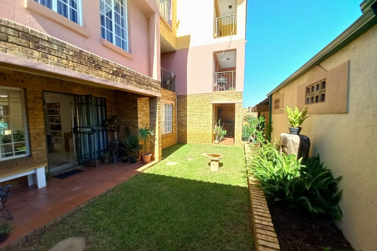 A rear view of the townhouse featuring a private garden, a tiled patio area, and multi-level balconies with brick exterior finishes.