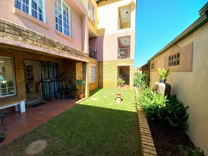 A rear view of the townhouse featuring a private garden, a tiled patio area, and multi-level balconies with brick exterior finishes.