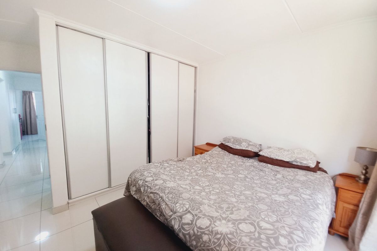 A bedroom featuring white tiled flooring and a large built-in sliding door wardrobe with a clean, neutral aesthetic.