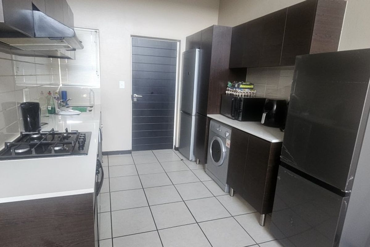 Modern galley-style kitchen featuring dark wood cabinetry, stone countertops, gas hob, extractor fan, and tiled flooring.