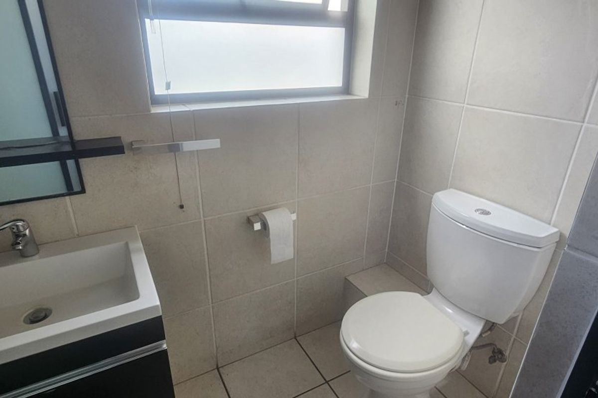 A clean, modern bathroom featuring a vanity cabinet with a ceramic basin, a wall-mounted mirror, and a standard toilet with tiled finishes.