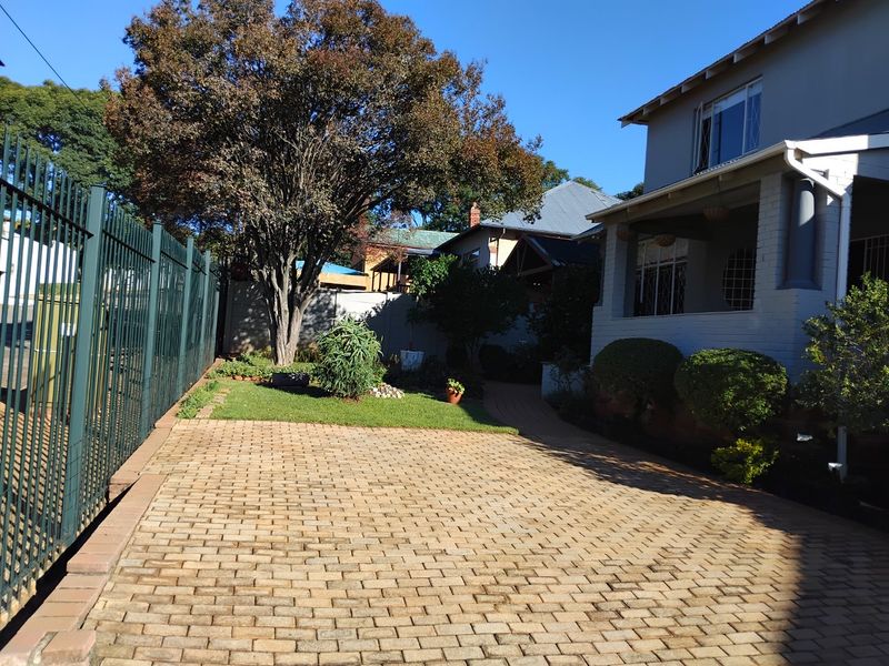 A well-maintained front exterior featuring a paved driveway, metal perimeter fencing, and a covered porch area with established garden landscaping.