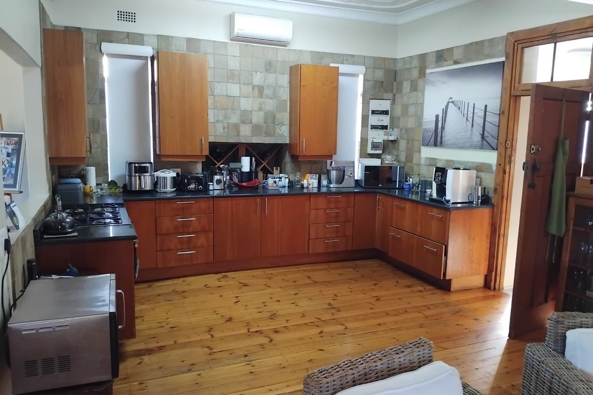 Spacious kitchen featuring warm wooden cabinetry, stone tile backsplash, gas hob, and hardwood flooring, offering a functional layout with integrated air conditioning.