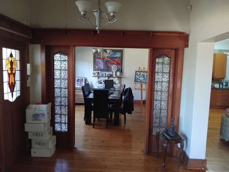 A living area featuring original timber flooring and decorative stained glass door frames, leading into a dining space with a fireplace mantel.