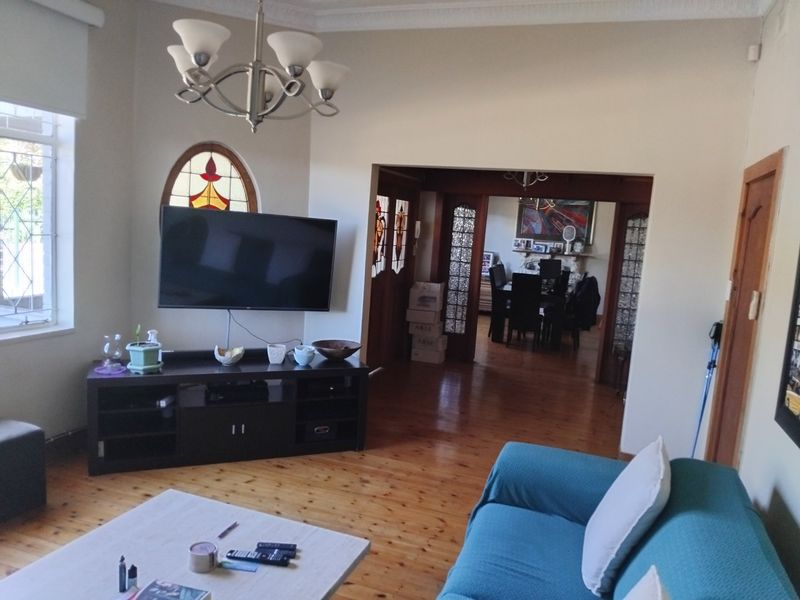 A living room featuring polished timber flooring, decorative cornicing, and a unique stained glass window, with an open flow into the adjacent dining area.