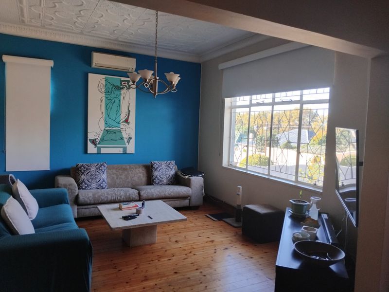 A living room featuring polished timber flooring, a decorative ceiling, and large windows with security bars, providing natural light and a view of the street.