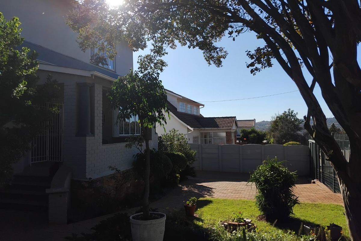 Rear exterior view of the property featuring a paved driveway, landscaped garden area, and a covered porch entrance.