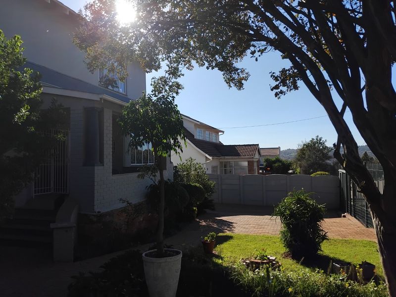 Rear exterior view of the property featuring a paved driveway, landscaped garden area, and a covered porch entrance.