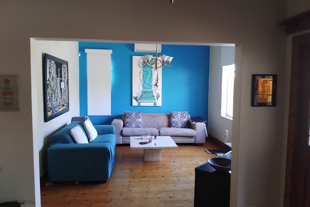 A living room featuring polished hardwood flooring, a bright blue accent wall, and a wall-mounted split-system air conditioner.