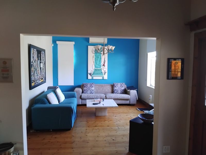 A living room featuring polished hardwood flooring, a bright blue accent wall, and a wall-mounted split-system air conditioner.