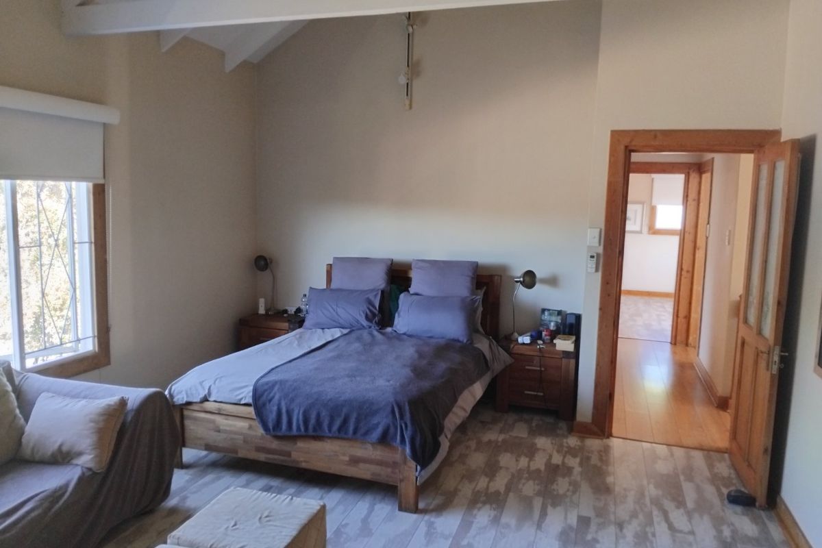 Spacious bedroom featuring exposed timber ceiling beams, laminate flooring, and natural light through a timber-framed window.