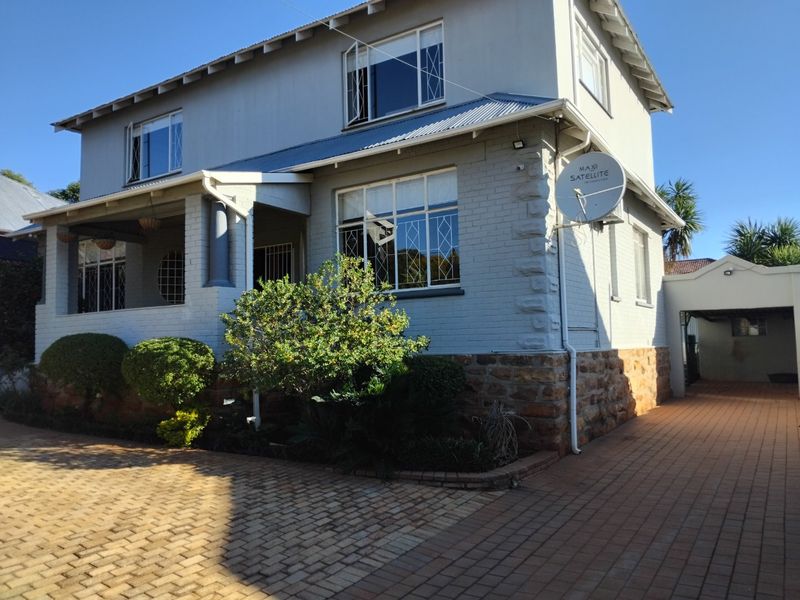 A well-maintained two-story house featuring a stone-clad base, brick driveway, covered porch, and secure window treatments.