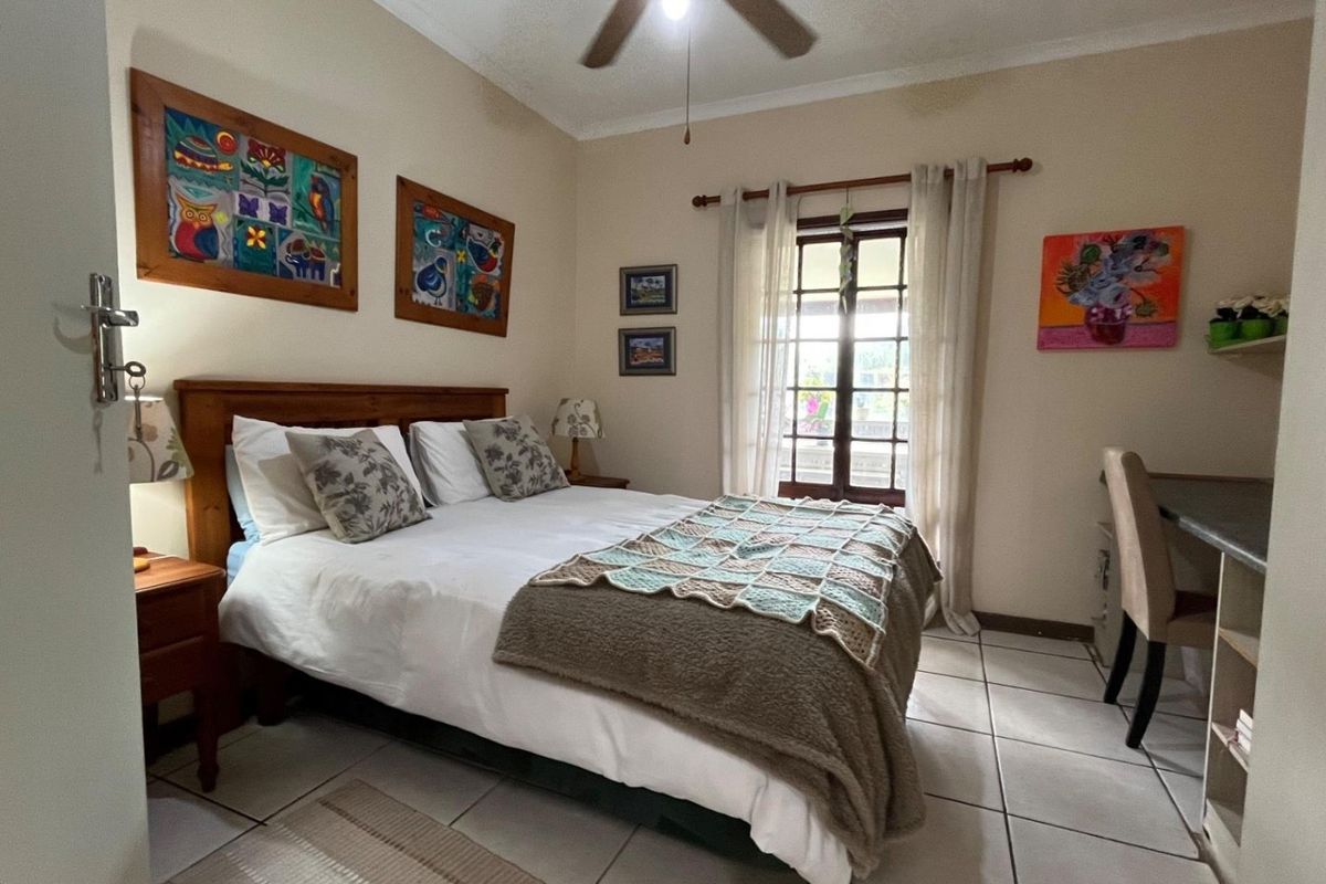 A cozy bedroom featuring tiled flooring, a ceiling fan, and direct access to the outdoors through classic french doors.