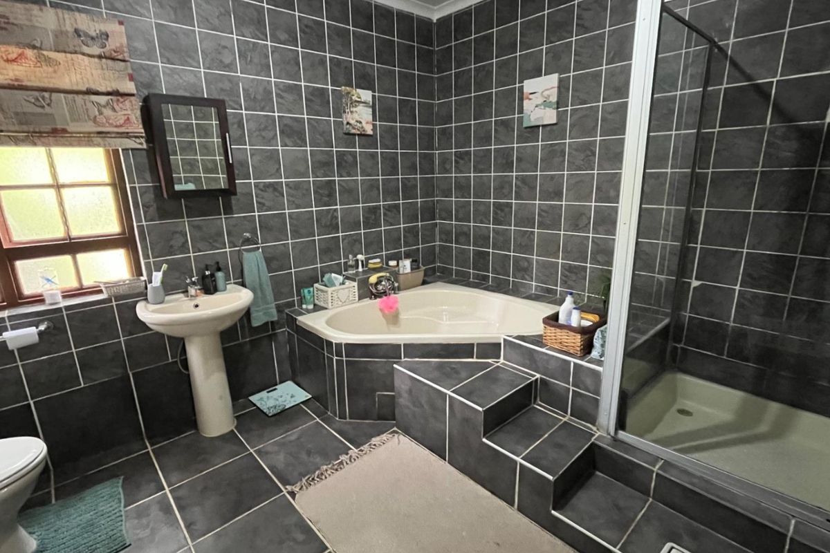 A bathroom featuring dark grey wall and floor tiles, a corner bathtub with steps, a separate shower enclosure, and a pedestal basin.