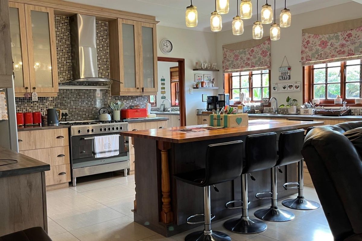 Spacious kitchen featuring a central island with a wooden countertop, gas stove, extractor fan, and mosaic tile backsplash, complemented by ample built-in cabinetry.