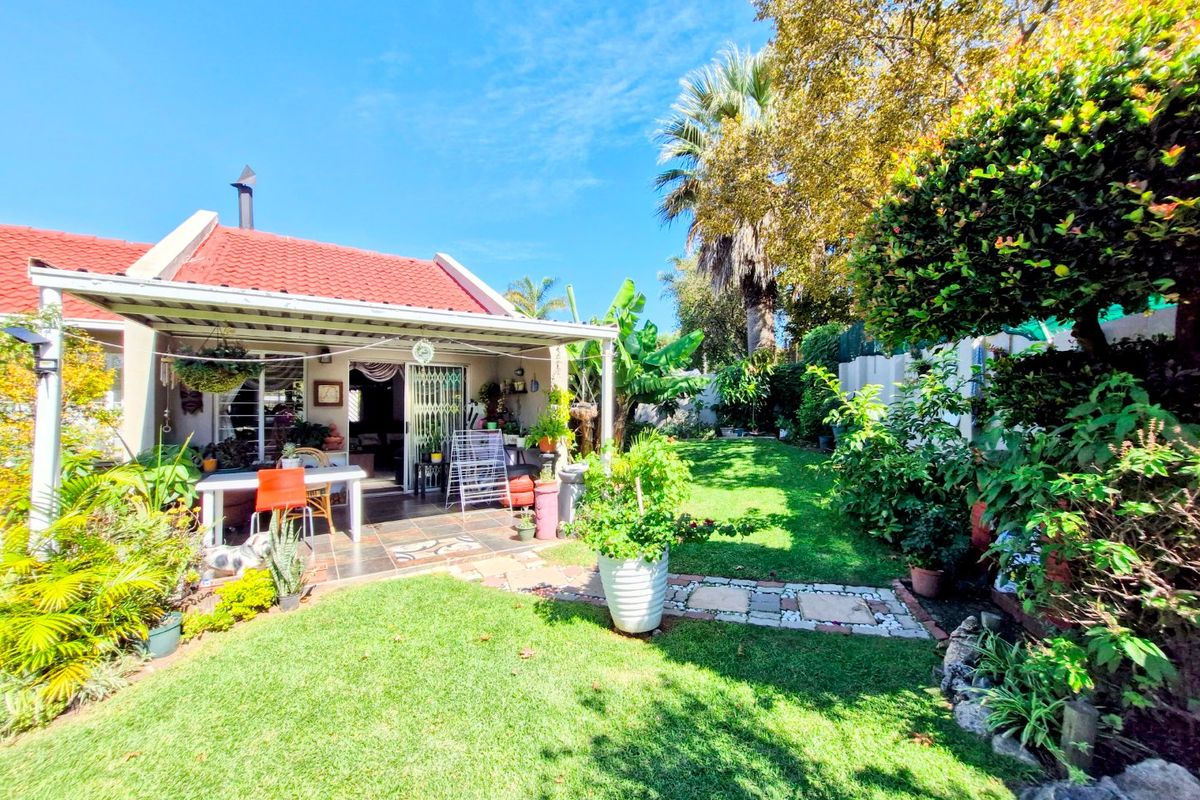 A well-maintained rear garden featuring a covered tiled patio, established landscaping, and a stone pathway leading through the lawn.