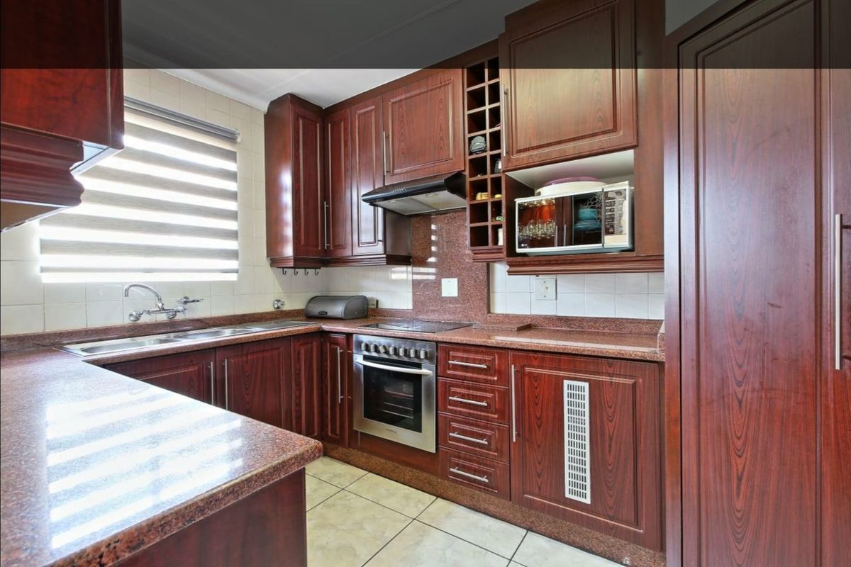 A well-maintained kitchen featuring dark wood cabinetry, granite countertops, built-in oven, electric hob, and integrated storage solutions.