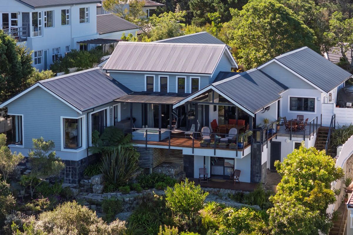 Aerial view of a multi-level residential property featuring a metal roof, timber decking, and a covered patio area set within a landscaped garden.