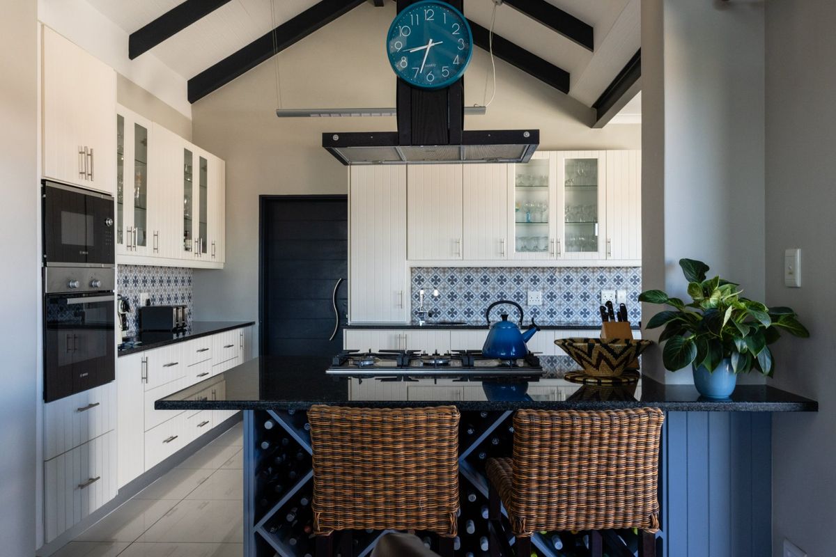 Modern kitchen featuring white cabinetry, granite countertops, a central island with a gas hob, built-in wine storage, and striking exposed ceiling beams.