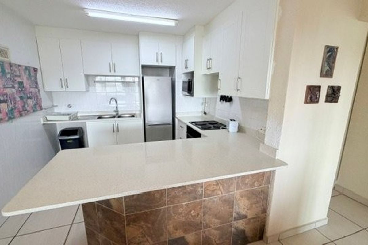 Functional kitchen featuring white cabinetry, stone countertops, a tiled breakfast bar, and integrated appliances, offering a practical layout for daily cooking and dining.