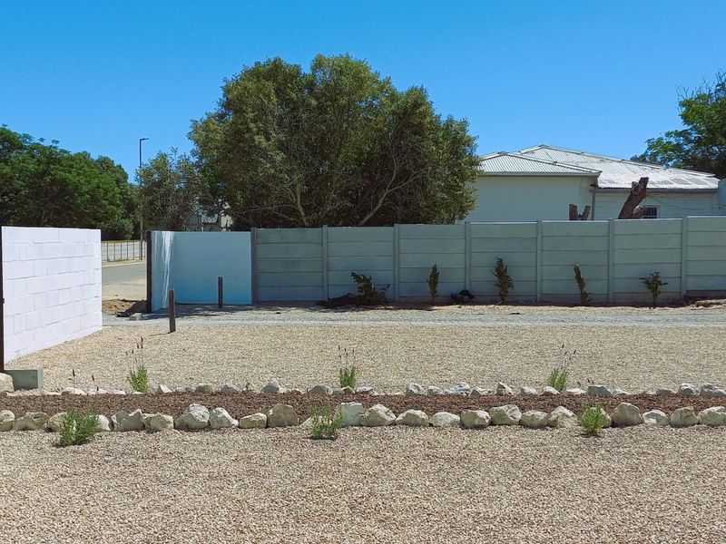 Front exterior view featuring a gravel driveway, concrete block boundary walls, and a timber pedestrian gate.