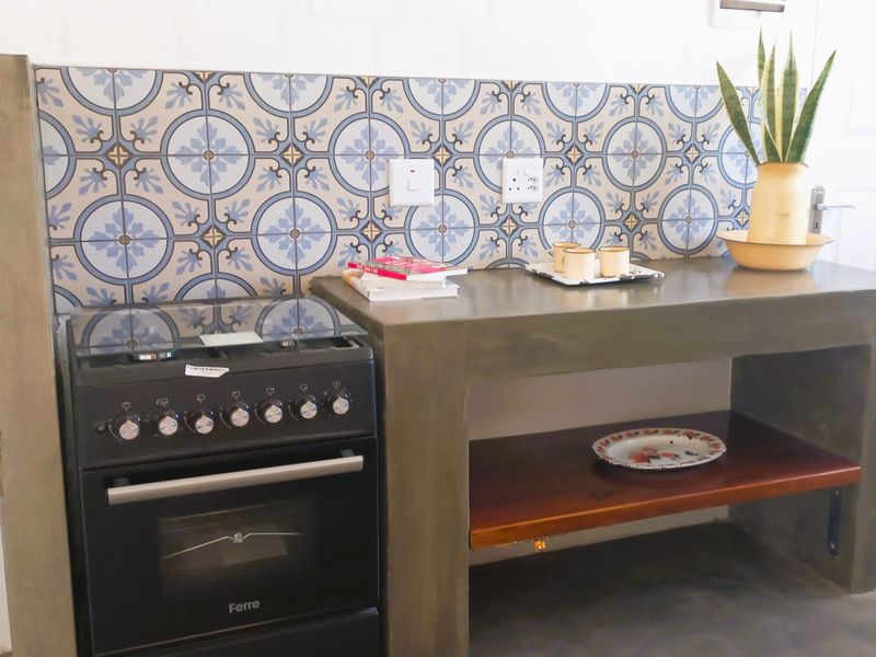 A compact kitchen area featuring a modern black gas stove, a concrete countertop with a decorative tile backsplash, and an integrated wooden storage shelf.
