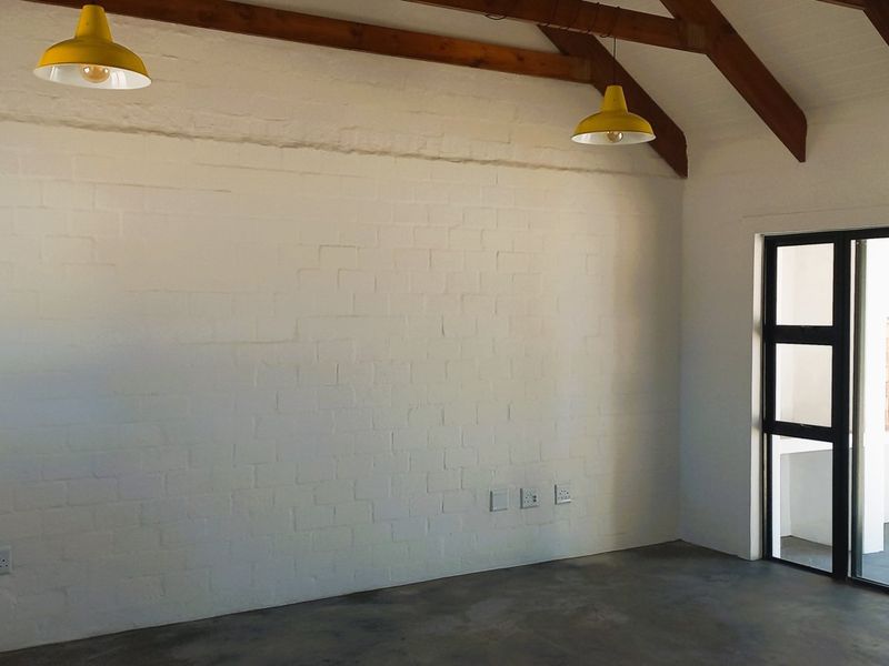 Spacious living area featuring exposed timber roof beams, painted brick walls, and polished concrete flooring, with direct access to an outdoor patio area.