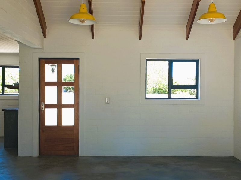 Bright and airy living space featuring exposed timber ceiling beams, painted brick walls, and polished concrete flooring with a classic timber entrance door.