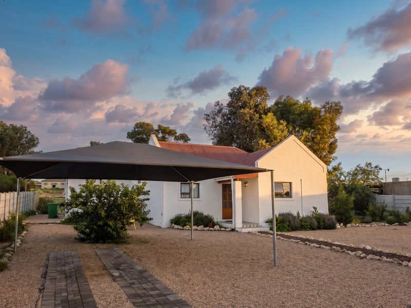 Front view of a white painted house featuring a corrugated metal roof, gravel landscaping, and a modern shade sail carport structure.