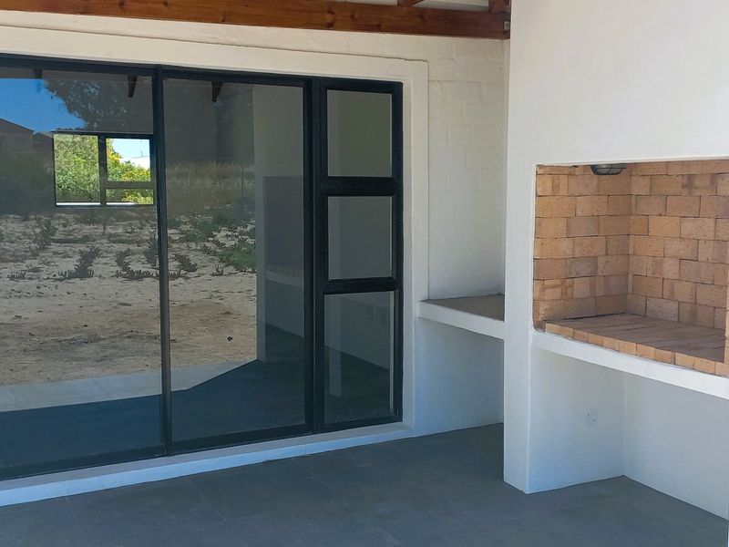 Covered patio area featuring a built-in brick braai, tiled flooring, and large sliding glass doors providing access to the interior.