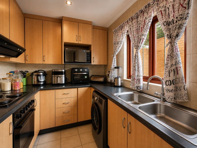 Functional kitchen featuring light wood cabinetry, dark laminate countertops, a double stainless steel sink, built-in oven, hob, and integrated laundry appliance.
