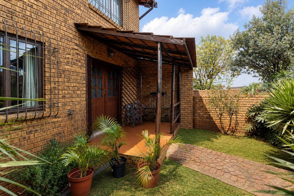 Rear exterior view of the townhouse featuring a face brick facade, a covered patio area, and a private garden with a paved walkway.