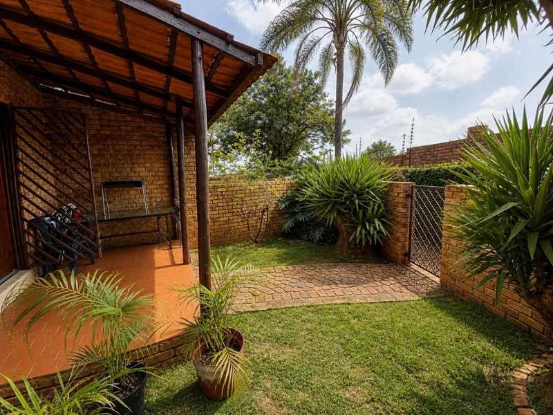 A covered brick patio area featuring a tiled floor and timber roof structure, leading out to a small private garden with brick boundary walls.