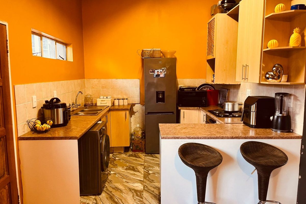 Compact kitchen featuring laminate cabinetry, tiled backsplash, breakfast bar, and built-in cooking appliances, requiring some cosmetic updates to the walls and flooring.