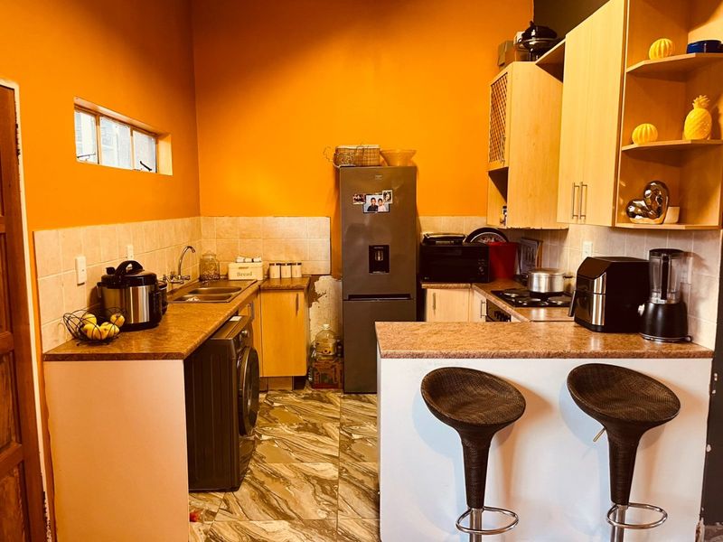 Compact kitchen featuring laminate cabinetry, tiled backsplash, breakfast bar, and built-in cooking appliances, requiring some cosmetic updates to the walls and flooring.