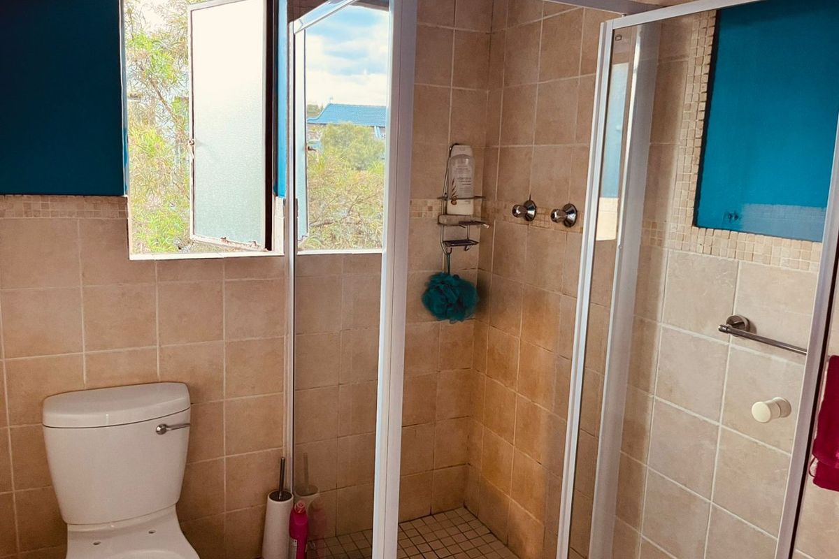 A functional bathroom featuring a shower enclosure, toilet, and tiled finishes, requiring cosmetic updates to improve its overall condition and aesthetic appeal.