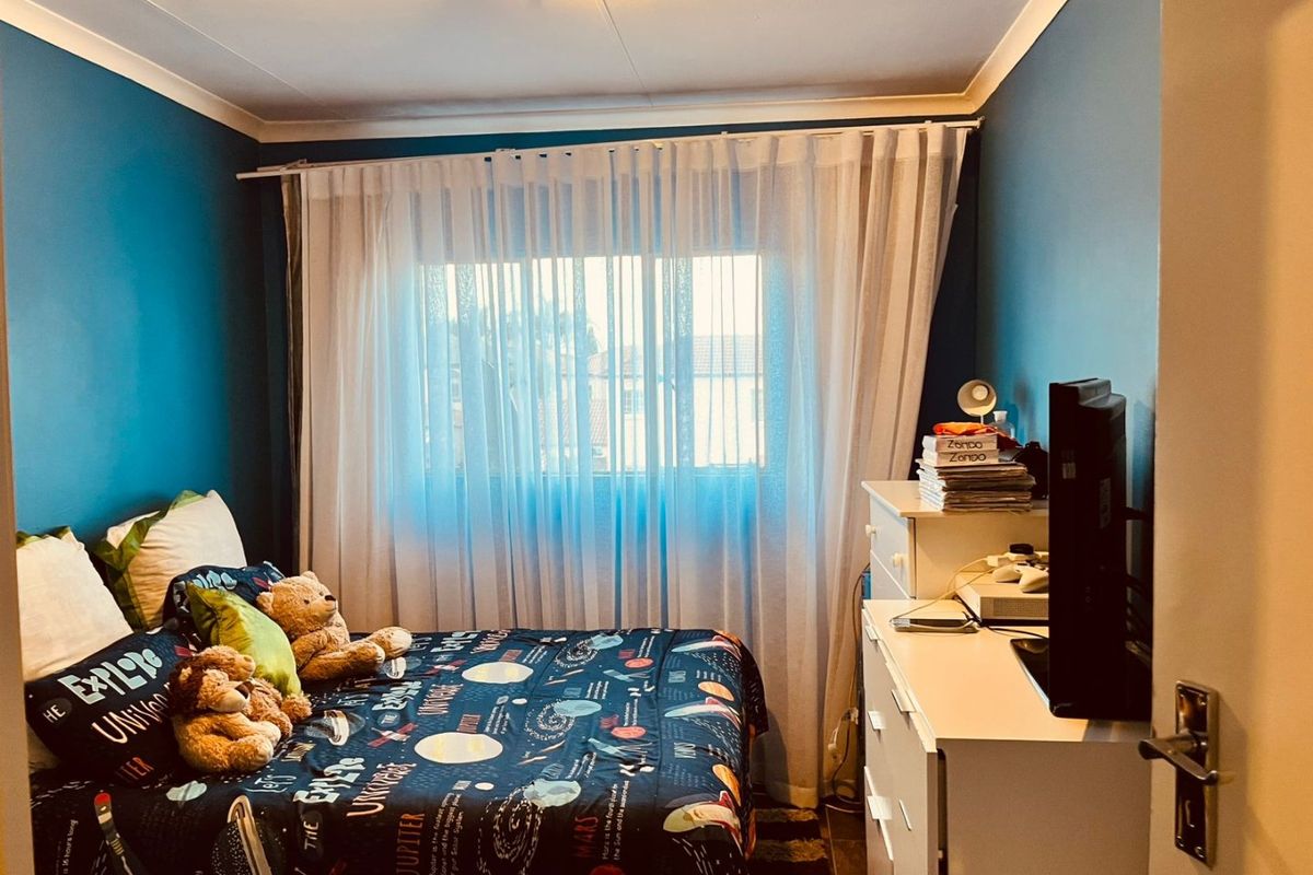 A cozy bedroom featuring blue painted walls, a window with sheer curtains, and a ceiling light fixture.