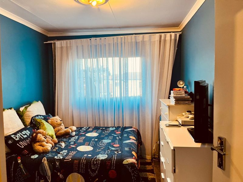 A cozy bedroom featuring blue painted walls, a window with sheer curtains, and a ceiling light fixture.