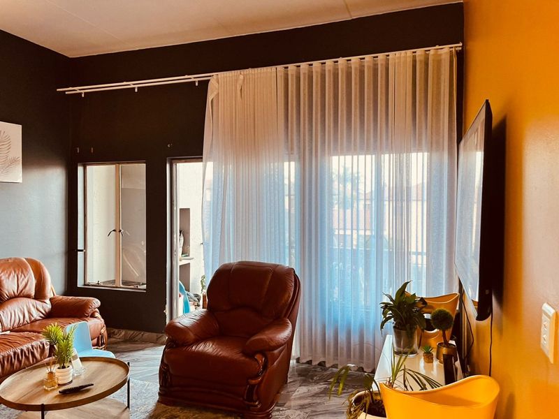 A living room featuring tiled flooring, a wall-mounted television, and large sliding doors with floor-to-ceiling curtains leading to an outdoor area.