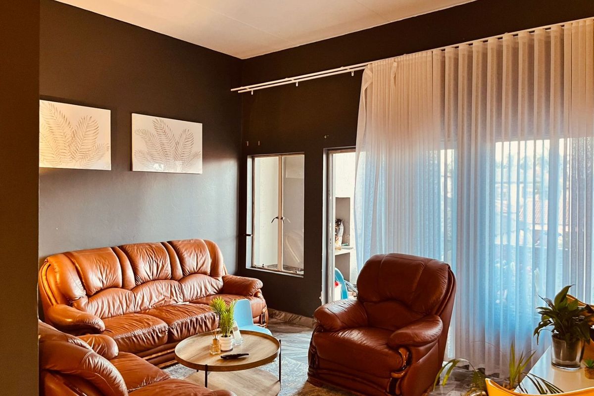 A living room featuring dark painted walls, large windows with sheer curtains, and access to an outdoor area through a sliding door.