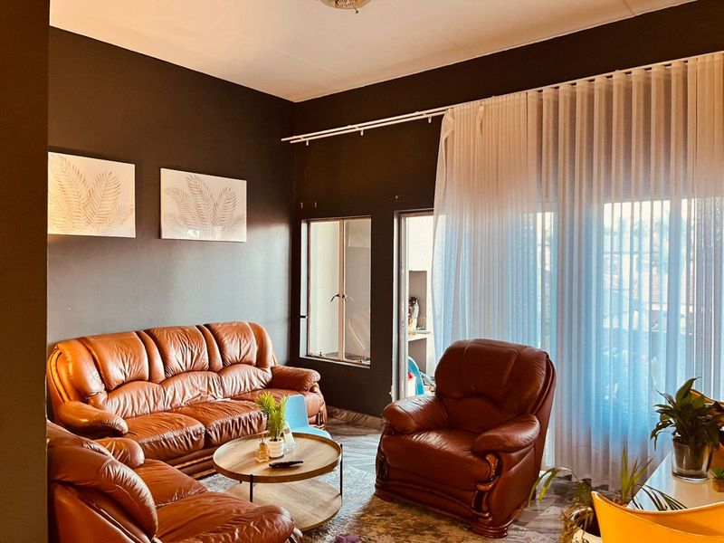 A living room featuring dark painted walls, large windows with sheer curtains, and access to an outdoor area through a sliding door.