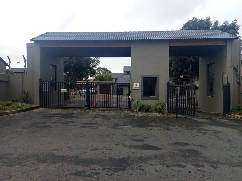 The main entrance to the apartment complex features a secure gated access point with a guard house, electric fencing, and a paved driveway.