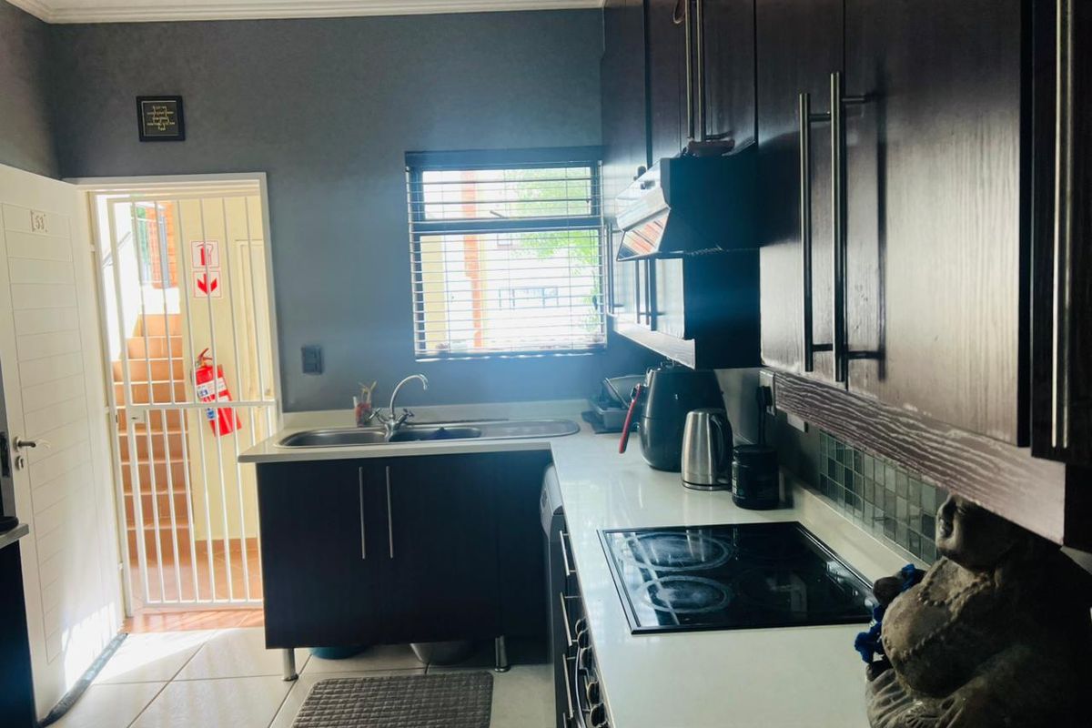 A functional kitchen featuring dark cabinetry, stone countertops, an integrated electric hob with extractor, and direct access to an exterior security gate.
