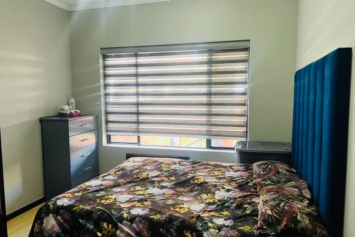 A well-maintained bedroom featuring laminate flooring, neutral wall tones, and modern roller blinds, providing a comfortable and functional living space.