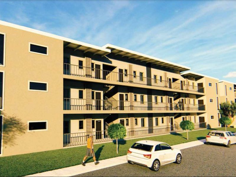 A modern multi-story apartment complex featuring clean architectural lines, private balconies with metal railings, and an adjacent paved driveway.