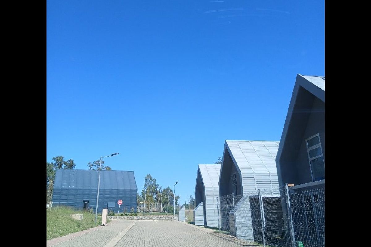 A view of a modern residential complex featuring houses with distinctive pitched roofs, metal cladding, and paved access roads.