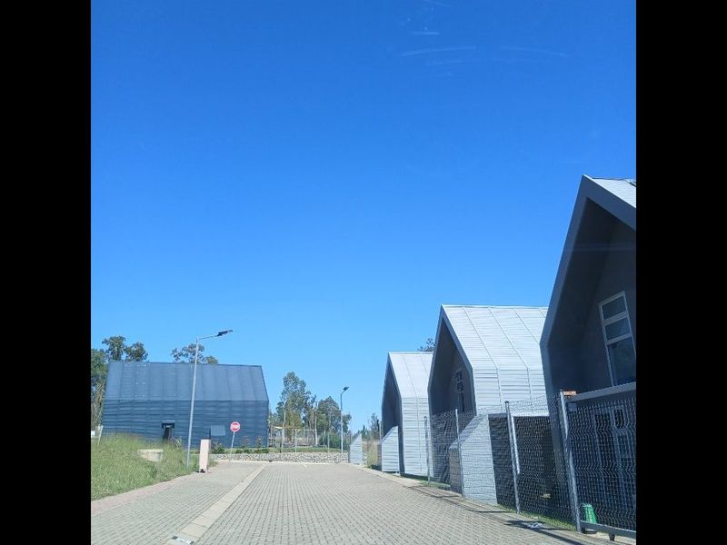 A view of a modern residential complex featuring houses with distinctive pitched roofs, metal cladding, and paved access roads.