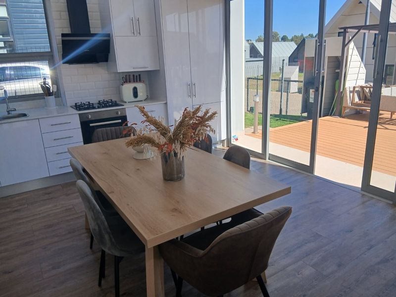 Modern open-plan kitchen and dining area featuring sleek white cabinetry, integrated appliances, and large sliding doors opening onto a wooden deck.